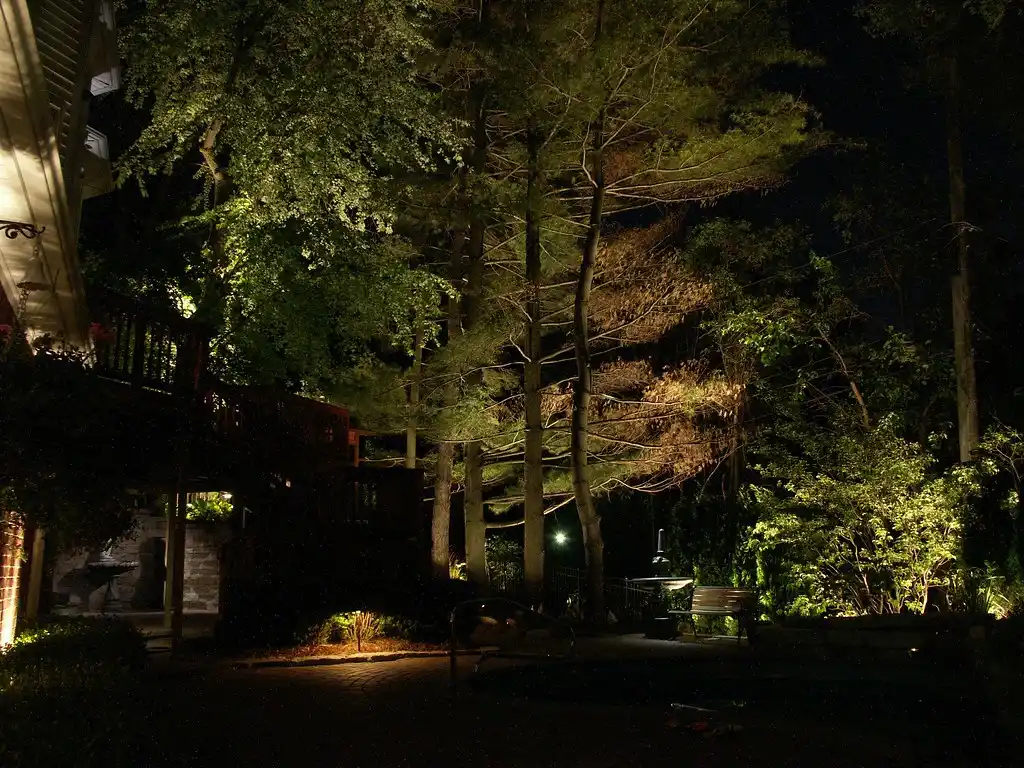 Hands marking a landscape lighting guide site map beside small outdoor fixtures and a measuring tape.