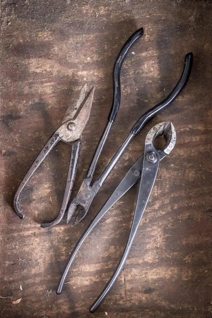 Hands wiring a bonsai branch with aluminum wire in a close-up workbench scene