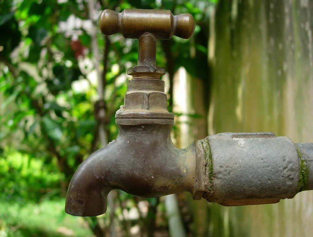 Hands connect different irrigation tubing sizes to a drip emitter near seedlings