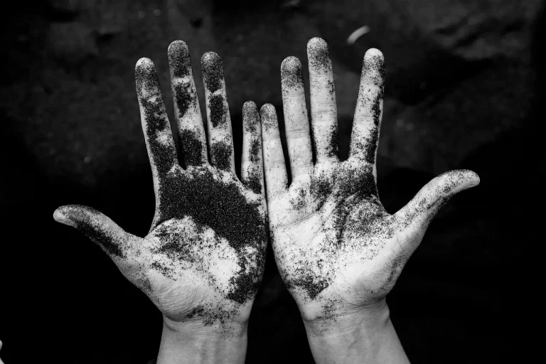 Gardener kneeling in a landscape bed, feeling a handful of moist soil to judge texture