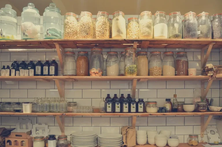 Home gardener sorts and stores seeds in jars and envelopes on a kitchen table with natural light.